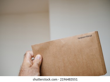 POV Male Hand Holding Paper Envelope With Inscription Hardware Plus Manual - White Wall Room Background