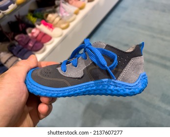 POV Male Hand Holding Small Blue Children Shoe With Multiple Colorful Shoes In Background