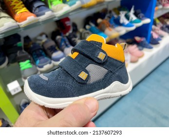 POV Male Hand Holding Small Blue Children Shoe With Multiple Colorful Shoes In Background