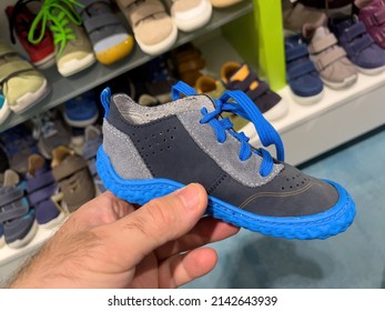 POV Male Hand Holding Small Leather Blue Children Shoe With Multiple Colorful Shoes In Background