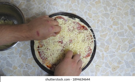 POV Male Hands Of Cook Putting Grated Cheese On Pastry With Ingredients In Metal Form At Cuisine. Chef Making A Pepperoni Pizza On Wooden Surface At Kitchen. Food Preparing Concept. Top View Slow Mo