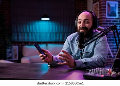 POV of male influencer reviewing smartphone product on camera, filming podcast video in studio with neon lights. Online vlogger doing mobile phone recommendation on internet livestream.