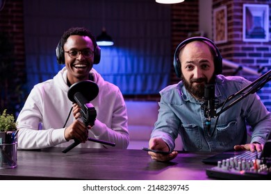 POV of male influencers recording podcast chat on camera, using streaming equipment in studio with neon lights. Content creators having fun filming online episode for social media.