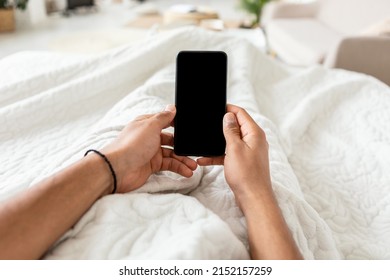 POV Of Man Using Mobile Phone With Empty Screen Texting And Browsing Internet, Holding Cellphone In Hands Lying In Bed In Modern Bedroom Indoor. Great Application Concept. Cropped