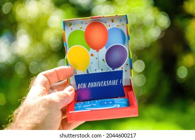 POV Personal Perspective Of Man Holding E-commerce 3-D Gift Card - Open And Bonne Anniversaire Signage In French Transalted As Happy Birthday