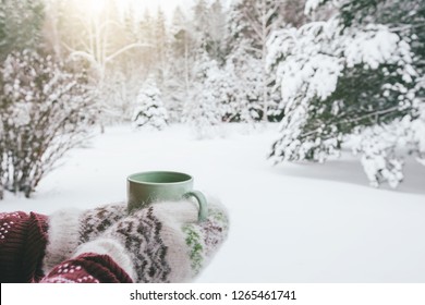 POV photo of mug with hot tea in human hand in mittens over snowy forest some winter morning - Powered by Shutterstock