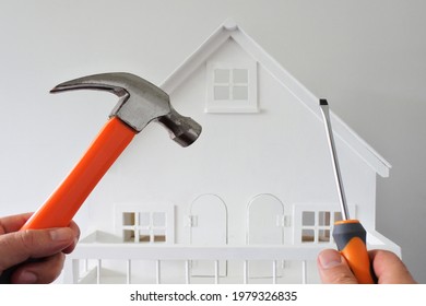 POV (point Of View) Of A One Person Holding A Hammer And Screwdriver Against A White House. Renovation, Home Decoration And Painting House Concept. No People. Copy Space