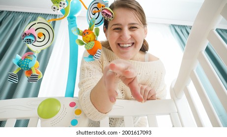 POV shot of baby looking on smiling mother playing with him in crib. Concept of parenting, family happiness and baby development.
