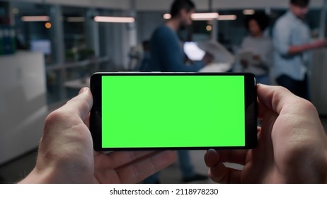 Pov shot of businessman using smartphone with blank green screen copy space in busy office. Employee holding cellphone working in coworking space  - Powered by Shutterstock