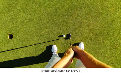 Pov shot of golf player at the putting green hitting ball into a hole. Personal perspective of professional golfer playing golf on field.