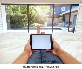 POV Shot Of Man Using Digital Tablet While Lying On Bed. Human Hand Holding Digital Tablet With Blank Screen.