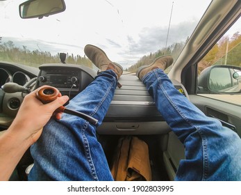 POV Shot Of Photographer's Feet And Legs Resting On The Dashboard Of Car Running Across A Secondary Road In The Countryside.