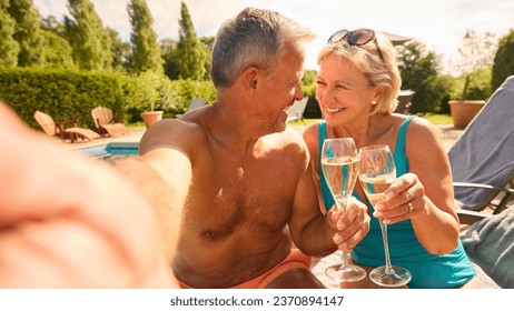 POV Shot Of Senior Couple On Holiday Posing For Selfie Drinking Champagne Relaxing By Swimming Pool - Powered by Shutterstock