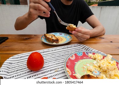 POV Shot Of A Skinny White Man Eating Using Fork With Raw Tomato, Scrambled Eggs And Bread Toasts On A Tray.  Sharing A Nutritious Breakfast With Boyfriend Or Couple At Home Terrase Concept.