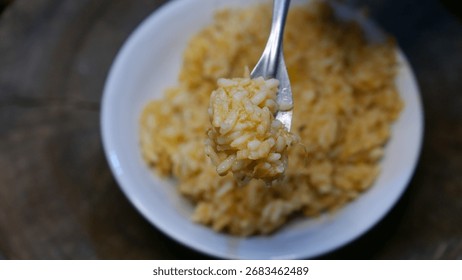 POV: Someone eating risotto with a fork. A plate of risotto on the table. A close-up shot.