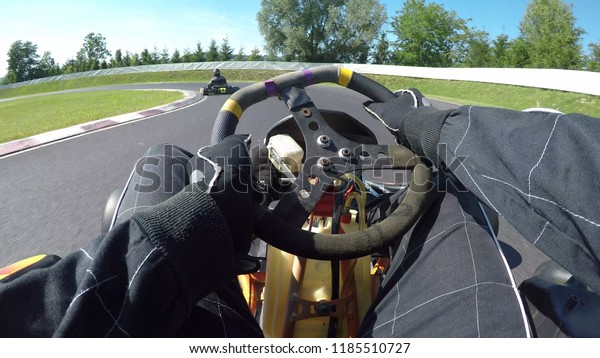 POV: Steering a speeding go cart along the winding\
asphalt circuit on a sunny autumn day. Driving a fast cart in a\
black suit through sharp turns of a bumpy racetrack. Bright sun\
shines on racers