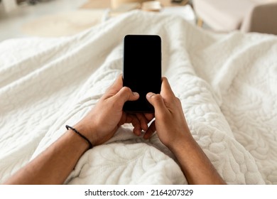 POV Of Unrecognizable Guy Holding Cellphone With Empty Screen Using Application And Texting Lying In Bed In Bedroom At Home. Great App For Your Smartphone, Gadgets Lifestyle Concept. Cropped