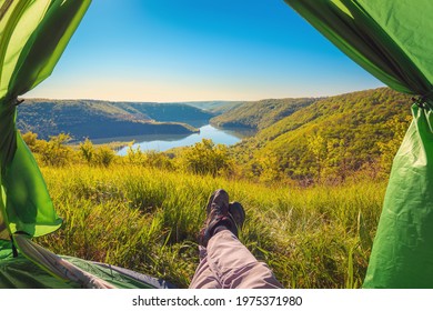 POV view, feet in the trekking shoes of the resting traveler in the camping tent, view to the mountain canyon and river, scenic nature background, adventure concept.