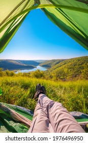 POV view, feet in the trekking shoes of the resting traveler in the camping tent, view to the mountain canyon and river, scenic nature background, adventure concept.