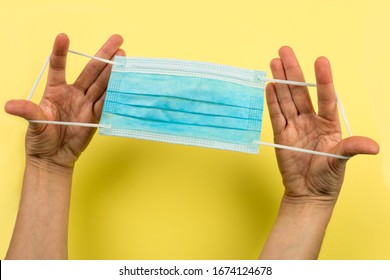 POV view of hands holding a medical mask by the elastic band, on a yellow background
