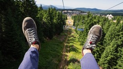 POV View Of Male Legs Going Down On  Ski Lift. Summer Outdoor Activity In The Mountains.