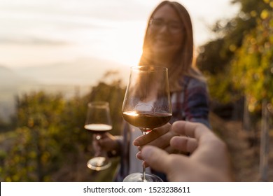 POV view of a woman who offers a glass of red wine to her friend in a vineyard during sunset - Powered by Shutterstock