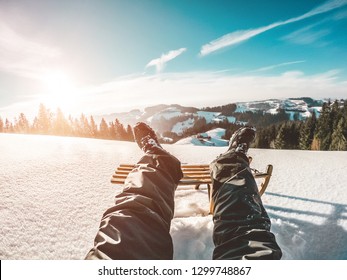 Pov View Of Young Man Looking The Sunset On Snow High Mountains With Vintage Wood Sledding - Legs View Of Travel Influencer Creating Content - Winter Vacation Concept - Focus On His Feet