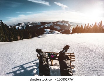 Pov View Of Young Man Looking The Sunset On Snow High Mountains With Vintage Sledding - Legs View Of Travel Influencer Enjoying Winter Landscape - Vacation Concept - Focus On Wood Luge