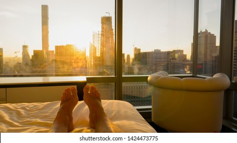 POV: Waking up to a spectacular golden sunrise illuminating the skyscrapers in downtown New York. Golden sunset shines through the window of your hotel room while you lie in your comfortable bed.