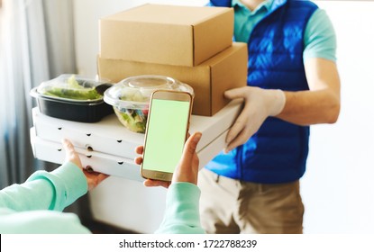 POV Of Woman Using Smarthone For Ordering Online, Receiving Takeout Food From Delivery Man. Courier Holding Paper Boxes And Containers. Delivery Food Service During Quarantine, Shopping Order Online