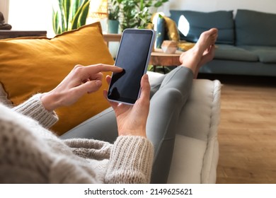 POV Of Young Caucasian Woman Using Mobile Phone Relaxing At Home In Cozy Living Room Apartment.