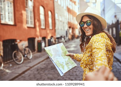 POV of a young woman holding a map and smiling while leading a person by the hand through city streets