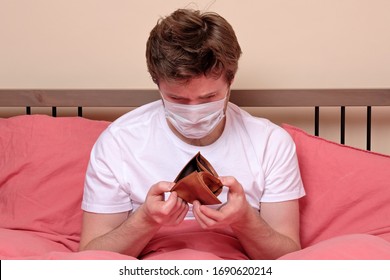 Poverty And Absence Of Money. Unemployed Sad Caucasian Man In Medical Mask Sitting At Home On Quarantine Or Isolation Because Of Covid Showing Empty Wallet. He Has No Money For Living.