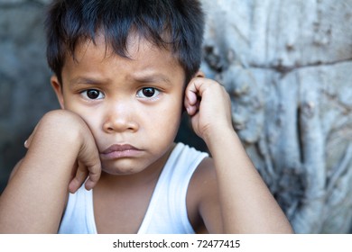 Poverty - portrait of a cute young Asian boy, Filipino male against wall with copyspace.