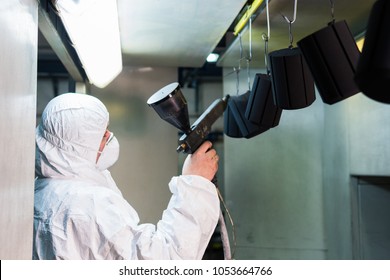 Powder coating of metal parts. A man in a protective suit sprays powder paint from a gun on metal products