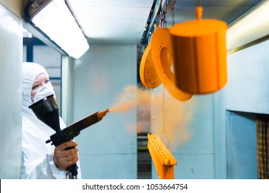 Powder coating of metal parts. A woman in a protective suit sprays powder paint from a gun on metal products