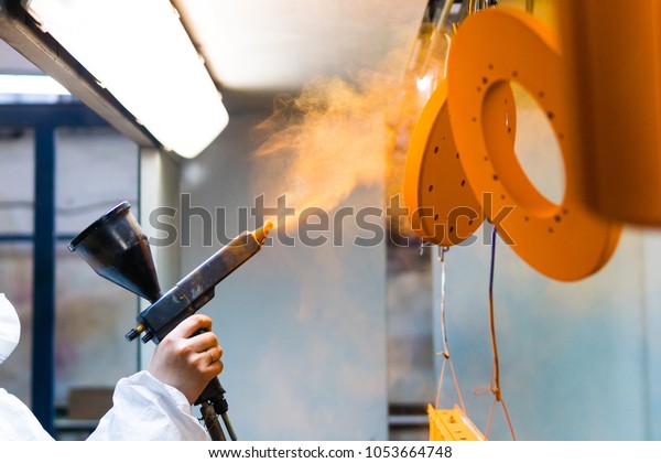 Powder coating of\
metal parts. A woman in a protective suit sprays powder paint from\
a gun on metal products