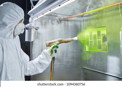 Powder coating of metal parts. Worker wearing protective wear performing powder coating of metal details in a special industrial camera. Hand holding powder coating sprayer