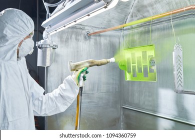 Powder coating of metal parts. Worker wearing protective wear performing powder coating of metal details in a special industrial camera. Hand holding powder coating sprayer