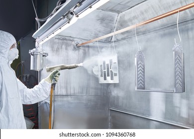 Powder Coating Of Metal Parts. Worker Wearing Protective Wear Performing Powder Coating Of Metal Details In A Special Industrial Camera. Hand Holding Powder Coating Sprayer