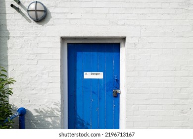 Powder-blue Hospital Generator Door Seen Within A Hospital Complex. A Generic Danger Sign Leads The Way To A Hospital Generator.