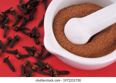 Powdered Clove Mortar With Pestle With Whole Cloves Close Up On Red Background