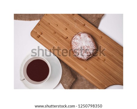 A powdered donut placed on a wooden chopping board surrounded with gold sprinkled stars. Black tea in a white tea cup and white saucer on the bottom left-hand side of the image. 