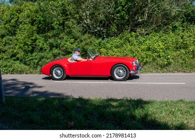 Powderham, Devon, Uk. July 9th 2022. Austin Healey Classic Car In Bright Red. Super Sexy Open Top British Sports Car From The 1960's. Pictured Driving Down A Country Road On A Summers Day.