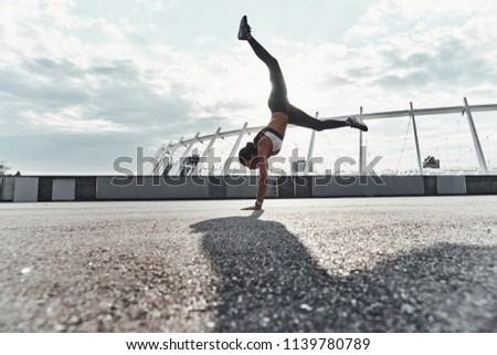 Power and balance. Full length of modern young woman in sports clothing doing handstand while exercising outdoors