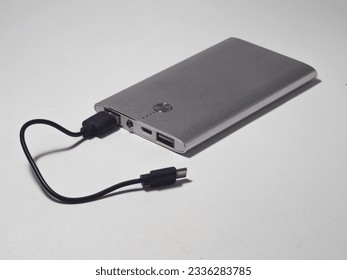 Power bank with an elegant design, silver in color with a black cable on a white background