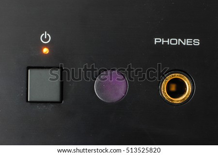 Power button, close-up in focus.  Minimal representation, square digital switch, led light and power sign, black polished metal .Infrared remote sensor and headphone jack. Audio Amplifier Knobs. 