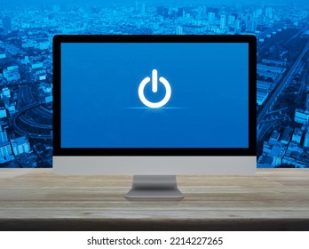 Power Button Icon On Desktop Modern Computer Monitor Screen On Wooden Table Over City Tower, Street, Expressway And Skyscraper, Business Start Up Online Concept