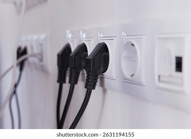 Power cables connected to electrical sockets on a wall