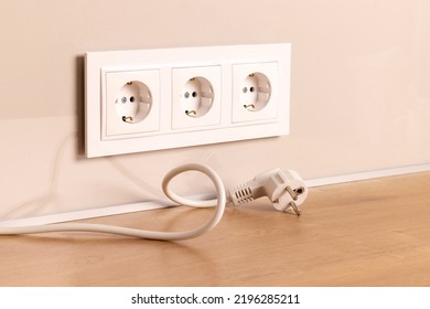 Power cord cable unplugged with group of white european electrical outlets on modern beige wall